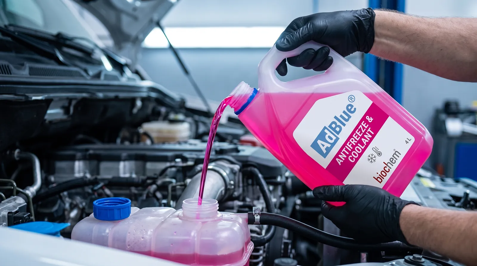 Gloved hands pouring pink AdBlue® Antifreeze & Coolant into an engine's coolant expansion tank